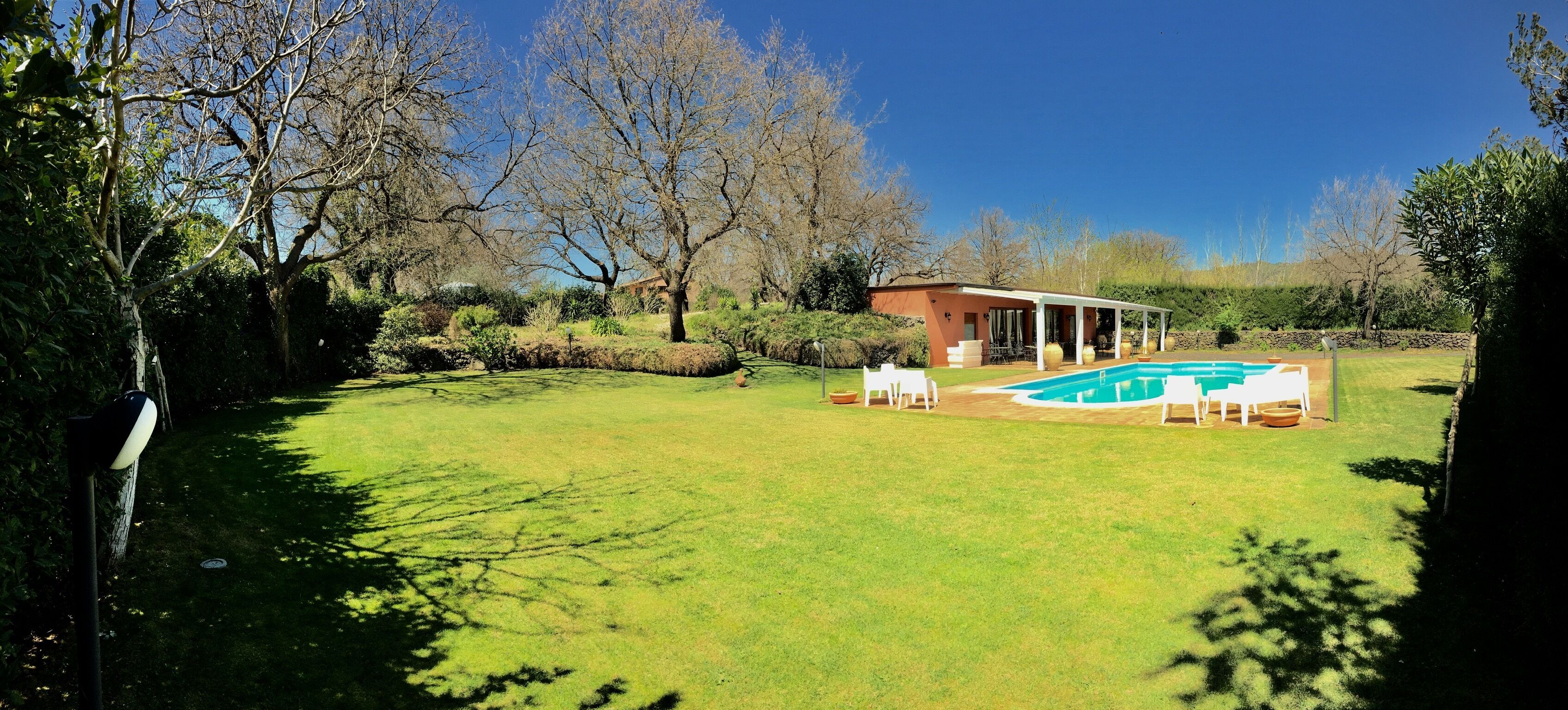 A backyard with a swimming pool, a covered patio, and a lawn.