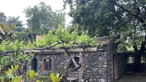 Ein rustikales Steinhaus mit einer Holzpergola, einer großen Vase und einer Bank im Hintergrund.