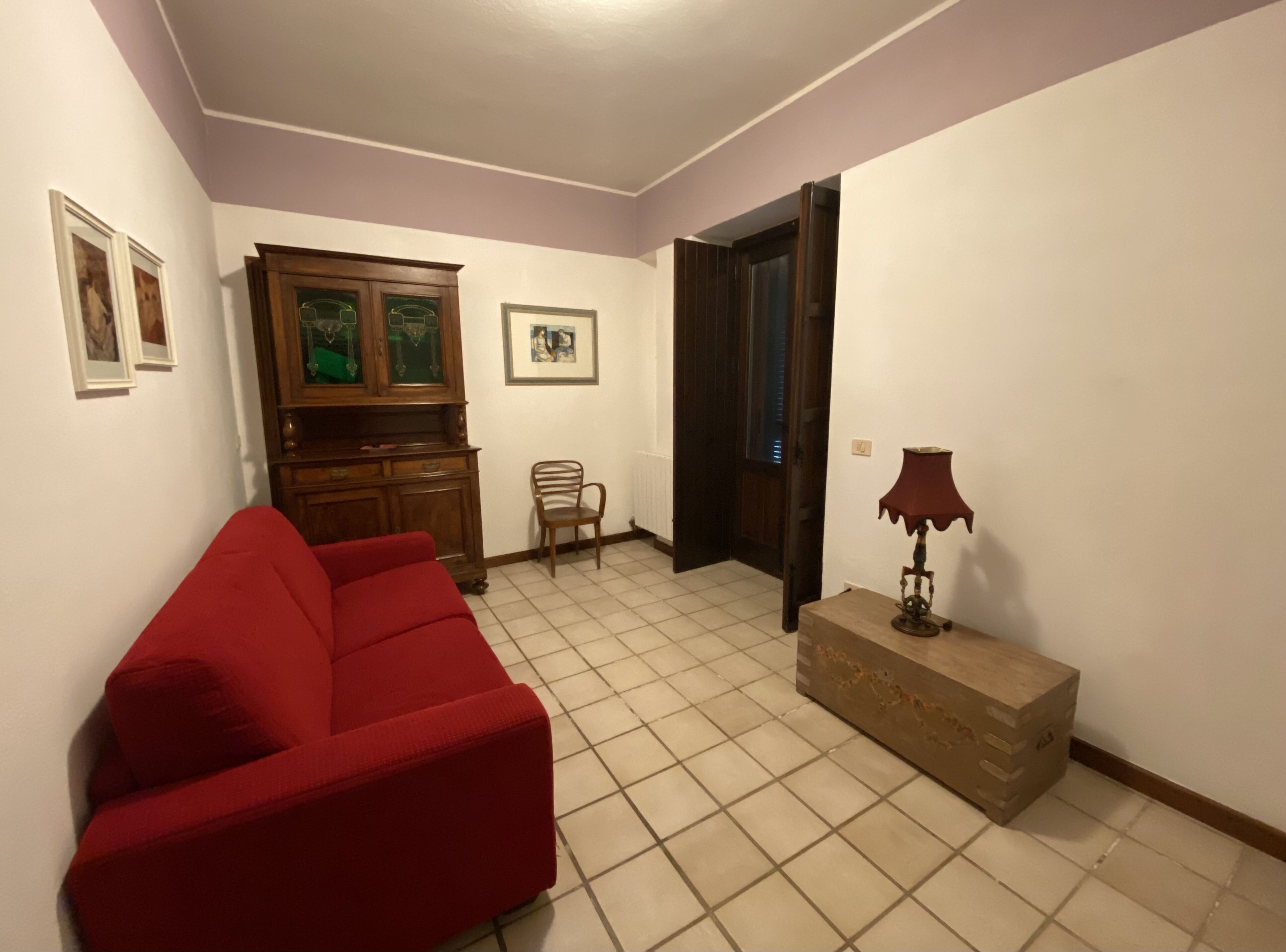 Uma sala de estar com um sofá vermelho, um armário de madeira, uma cadeira e um abajur.