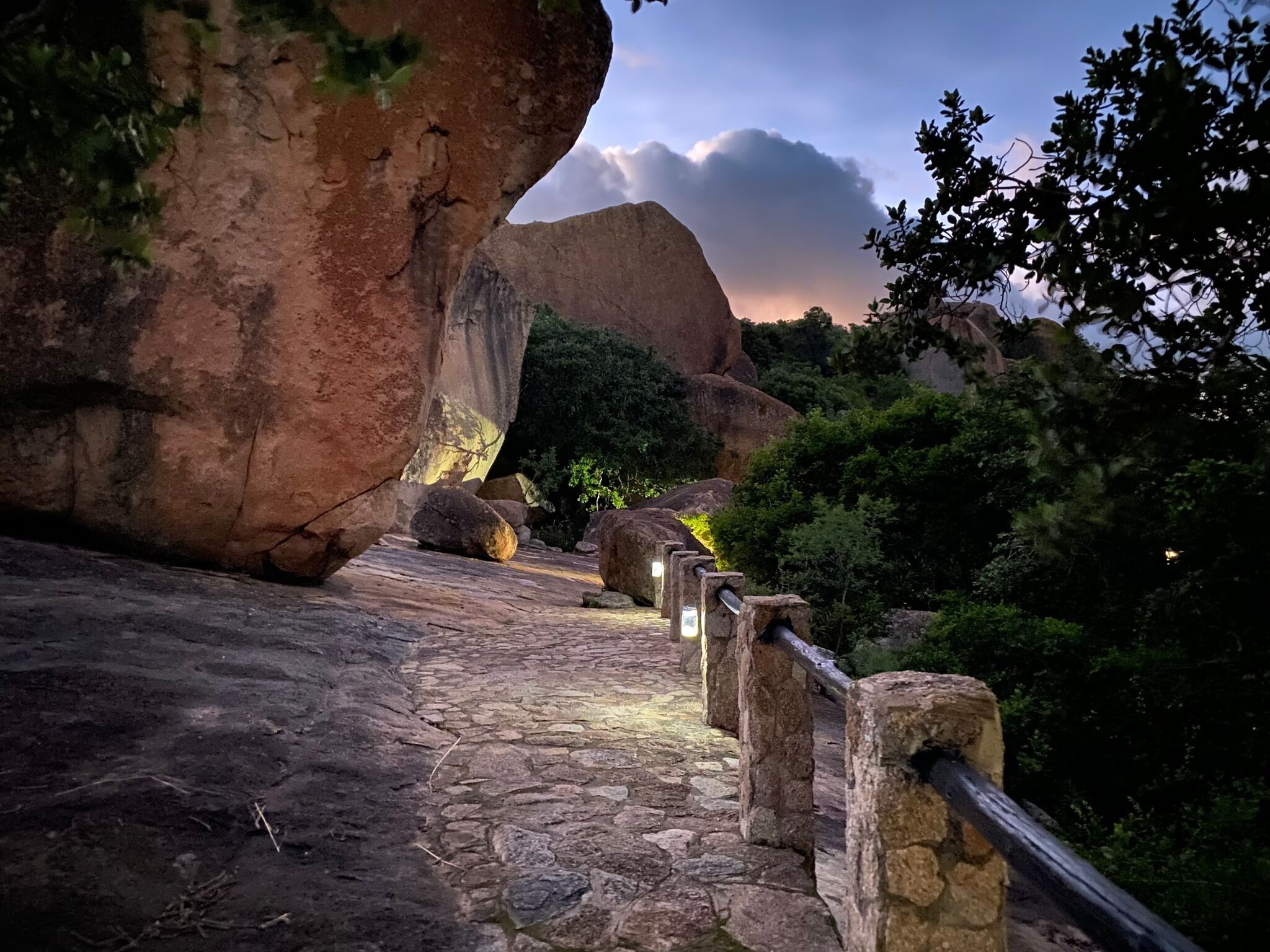 A stone pathway with a railing, surrounded by large rock formations and greenery.
