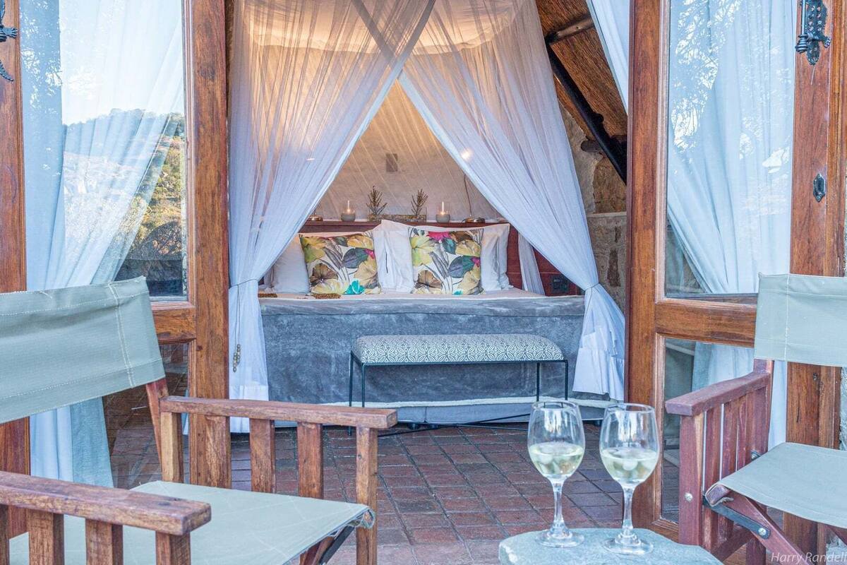 A cozy bedroom with a canopy bed, a stone bench, and a table with glasses.