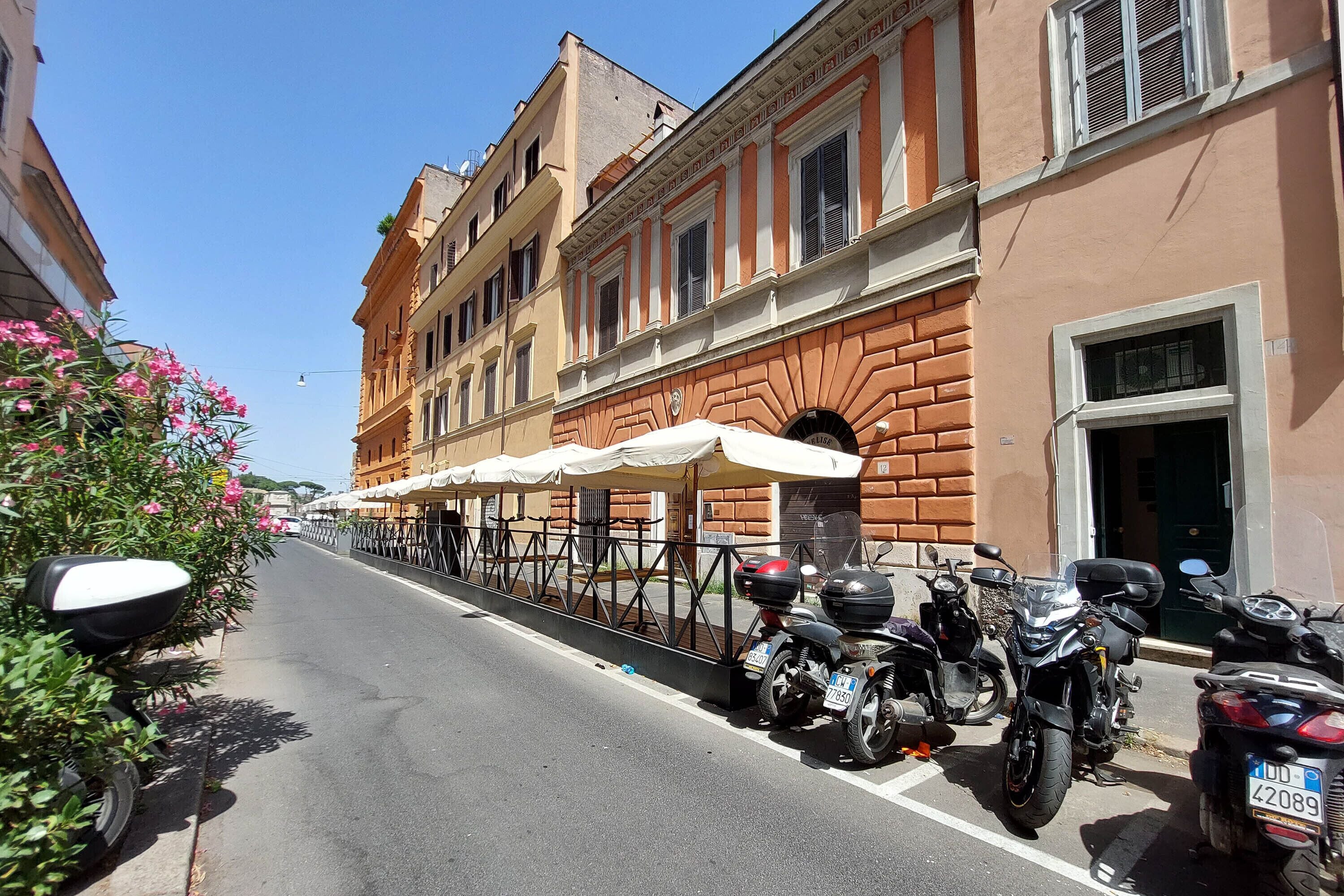 A street with parked motorcycles and a building with a brick facade and white awnings.