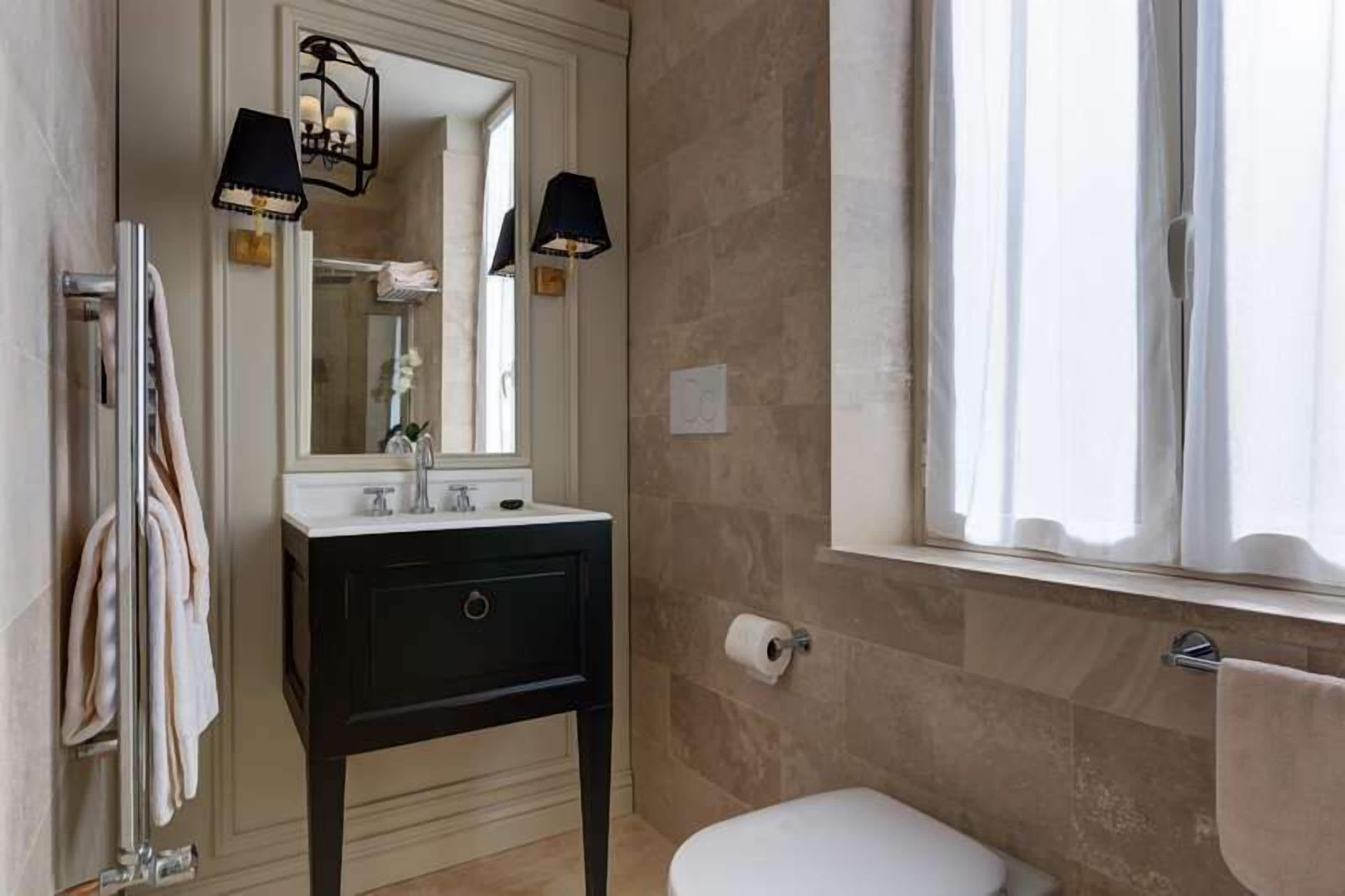 Un baño con un inodoro blanco, un tocador negro con espejo y dos lámparas de pared.