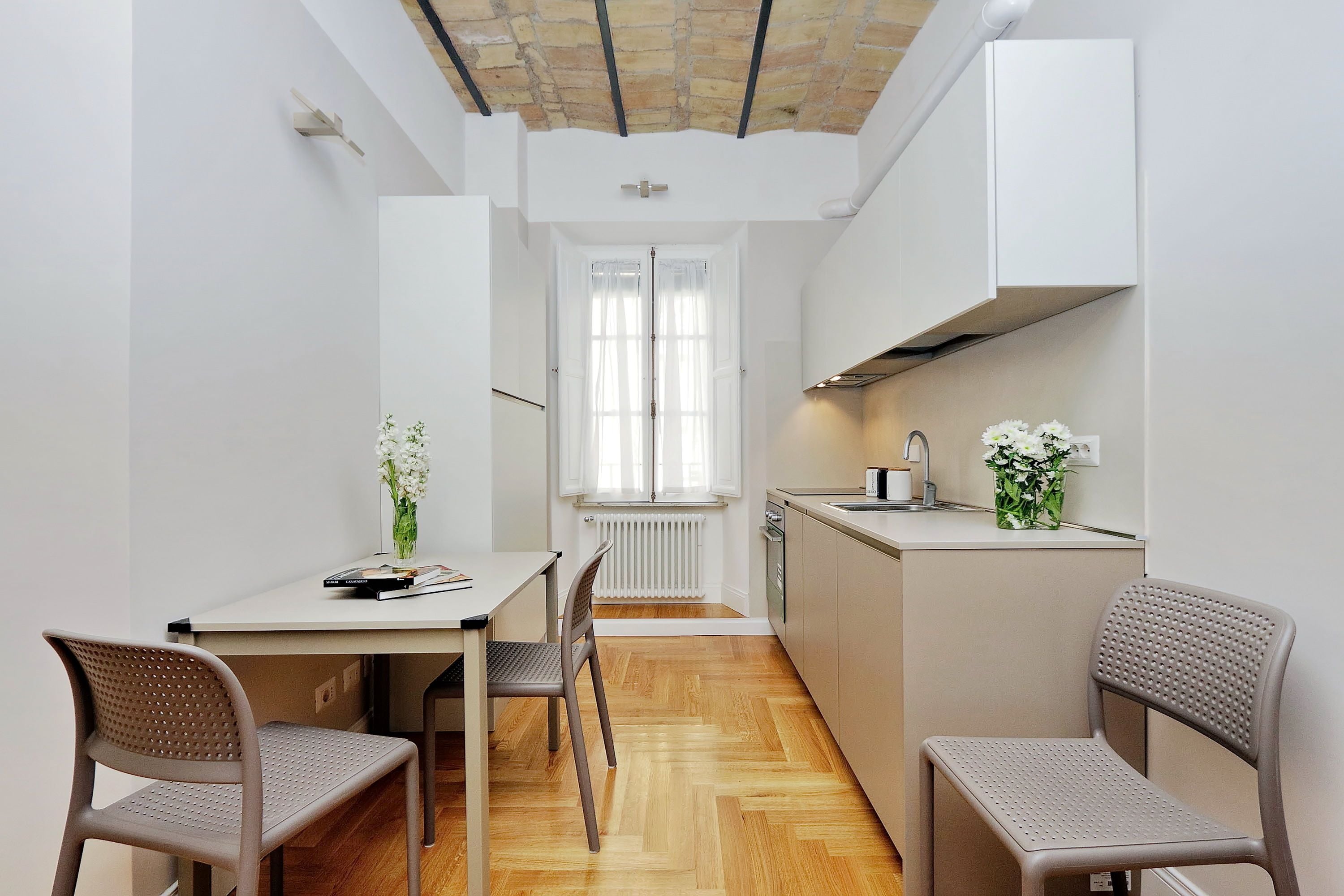Une cuisine moderne avec un coin repas, dotée d’un parquet en bois disposé en chevrons, de meubles blancs et d’un îlot central.