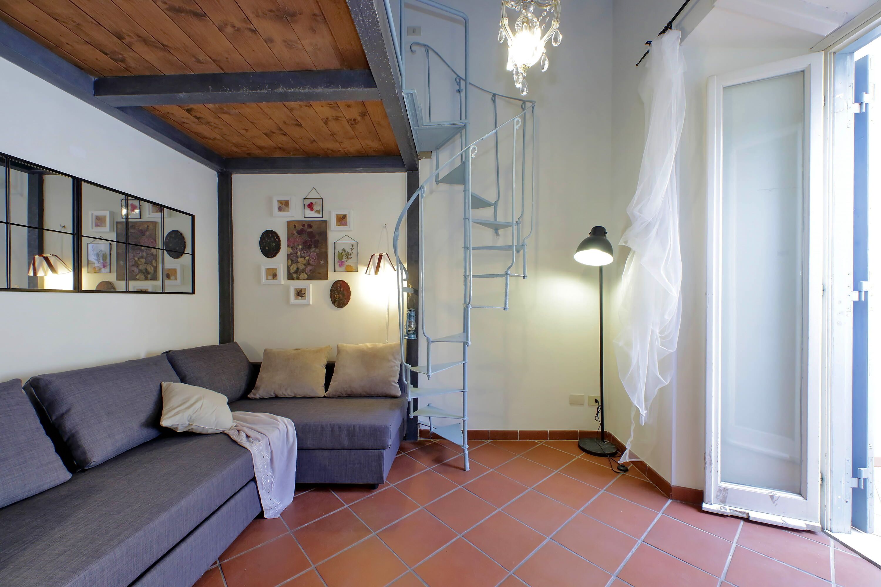 Un salon avec un canapé gris, un escalier et une porte donnant sur l’extérieur.