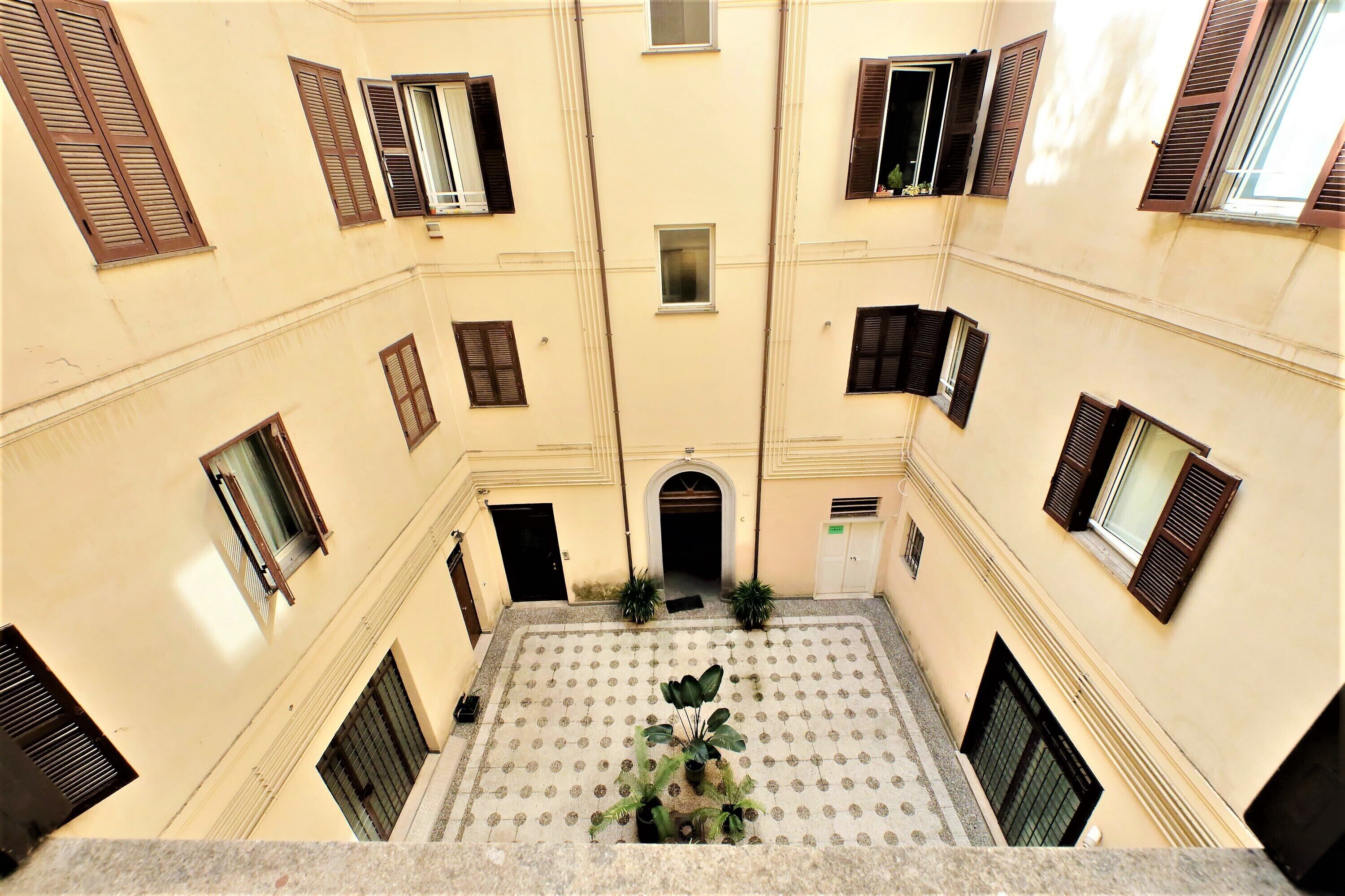 A courtyard with a tiled floor, multiple windows with shutters, and a central archway.
