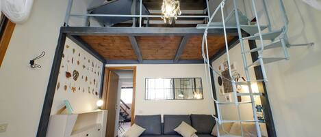 Quarto em estilo loft com um sofá cinza, um aparador branco e uma escada.