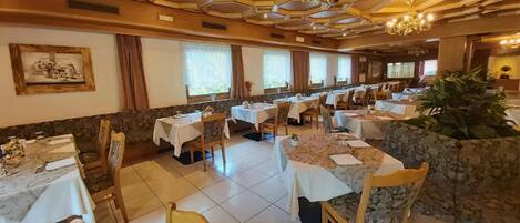 En matplats med flera bord och stolar, en kristallkrona och en vägg som är accentuerad med sten.