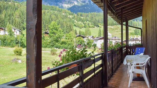 Un espacio exterior techado con una mesa y sillas, con vistas a un paisaje montañoso con casas y vegetación.