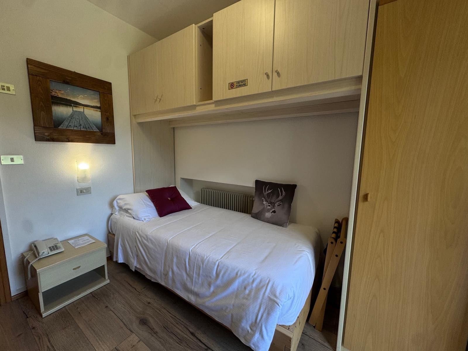 Ein Zimmer mit einem Einzelbett, einem Holzkopfteil, einem Nachttischtelefon und einem kleinen Tisch.