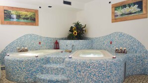 Un área de spa con dos jacuzzis, piso de mosaico azul y una planta pequeña en el centro.