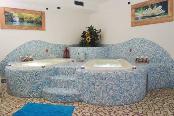 A spa area with two hot tubs, a blue mosaic floor, and a small plant in the center. - Hotel Scoiattolo (Falcade)