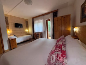 A bedroom with a large bed, a smaller bed, a wooden wardrobe, a television on the wall, and a window with curtains. - Hotel Scoiattolo (Falcade)