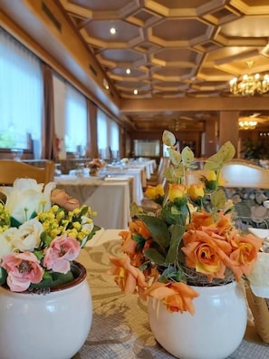 Comedor de hotel con mesas preparadas para el servicio, con centros de mesa florales en jarrones blancos.
