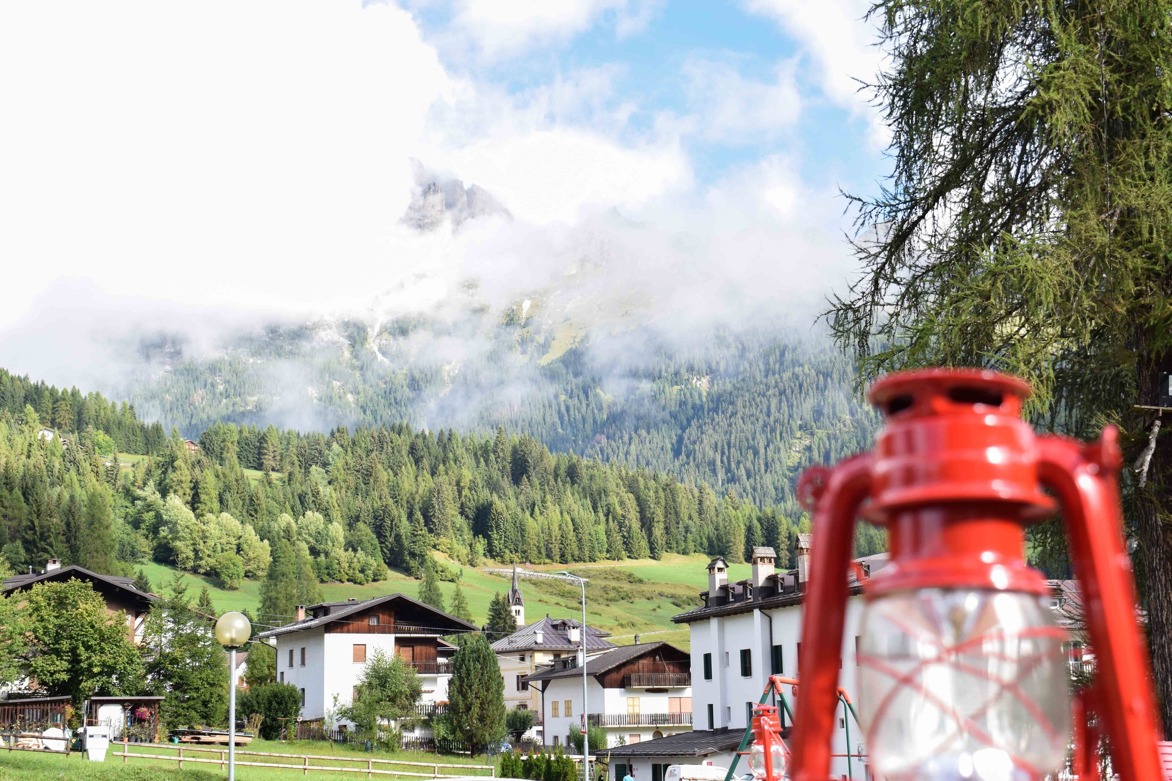 A mountain village with traditional houses, a clear sky, and a prominent mountain peak partially obscured by clouds.