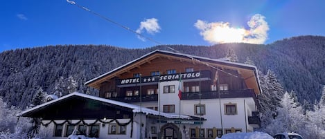 A hotel with a sign reading 'HOTEL S. COIATTTOLO' in front of a snowy mountain backdrop.