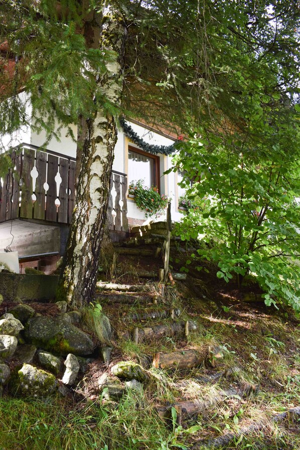 A traditional Japanese-style building with a wooden deck, surrounded by lush greenery and rocks. - Hotel Scoiattolo (Falcade)