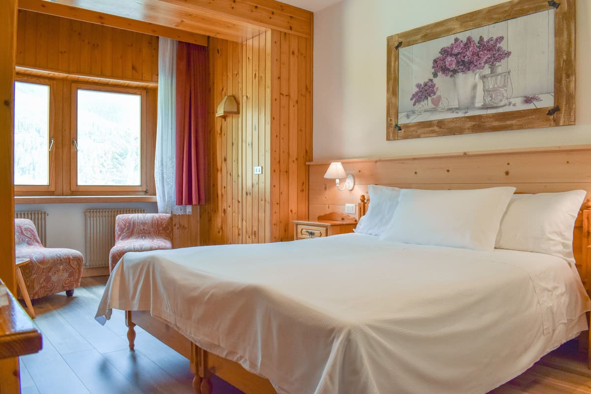 A wooden room with a bed, two chairs, a nightstand, and a wall-mounted lamp.