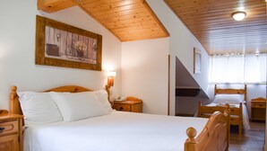 Un dormitorio con una cama de madera, una mesita de noche con lámpara, una mesita auxiliar de madera y un cuadro en la pared.