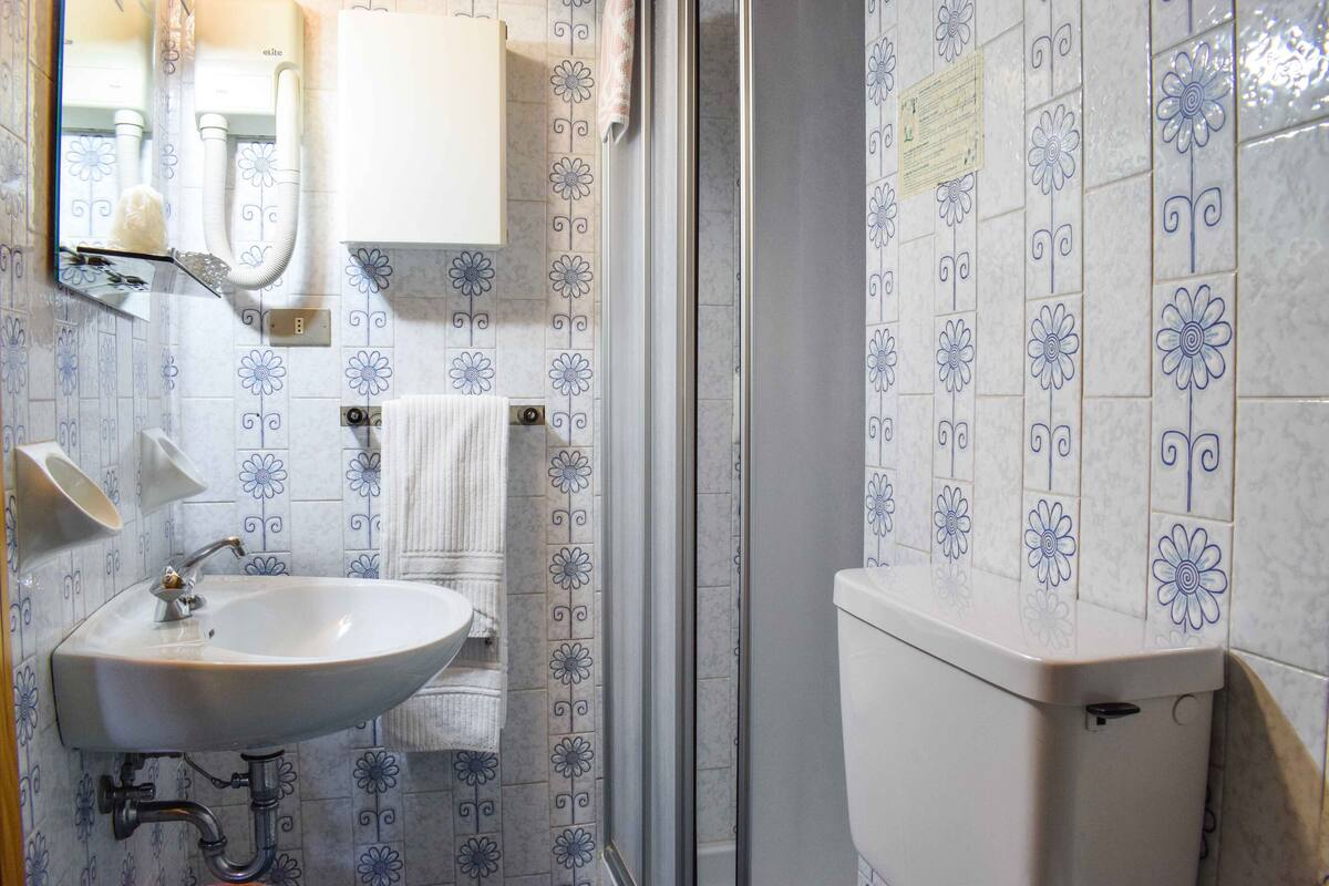 A bathroom with a white sink, mirror, and toilet, surrounded by blue and white floral tiles.