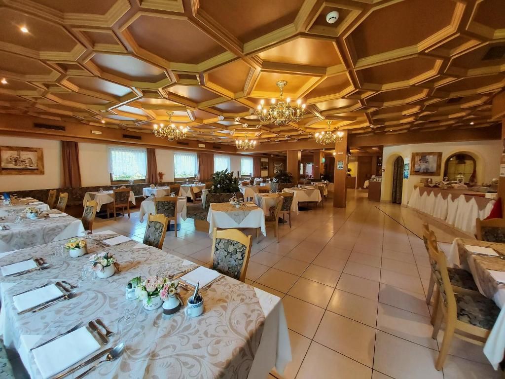 Un'ampia sala da pranzo con decorazioni a esagoni sul soffitto, lampadari e tavoli apparecchiati per consumare i pasti.