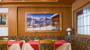 Un comedor con pared de madera, un ventanal grande y un cuadro de una escena montañosa nevada.