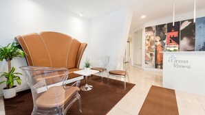 A modern lobby with a brown leather sofa, clear chairs, a small table, and a reception desk. - Ferrara Rooms (Ferrara)