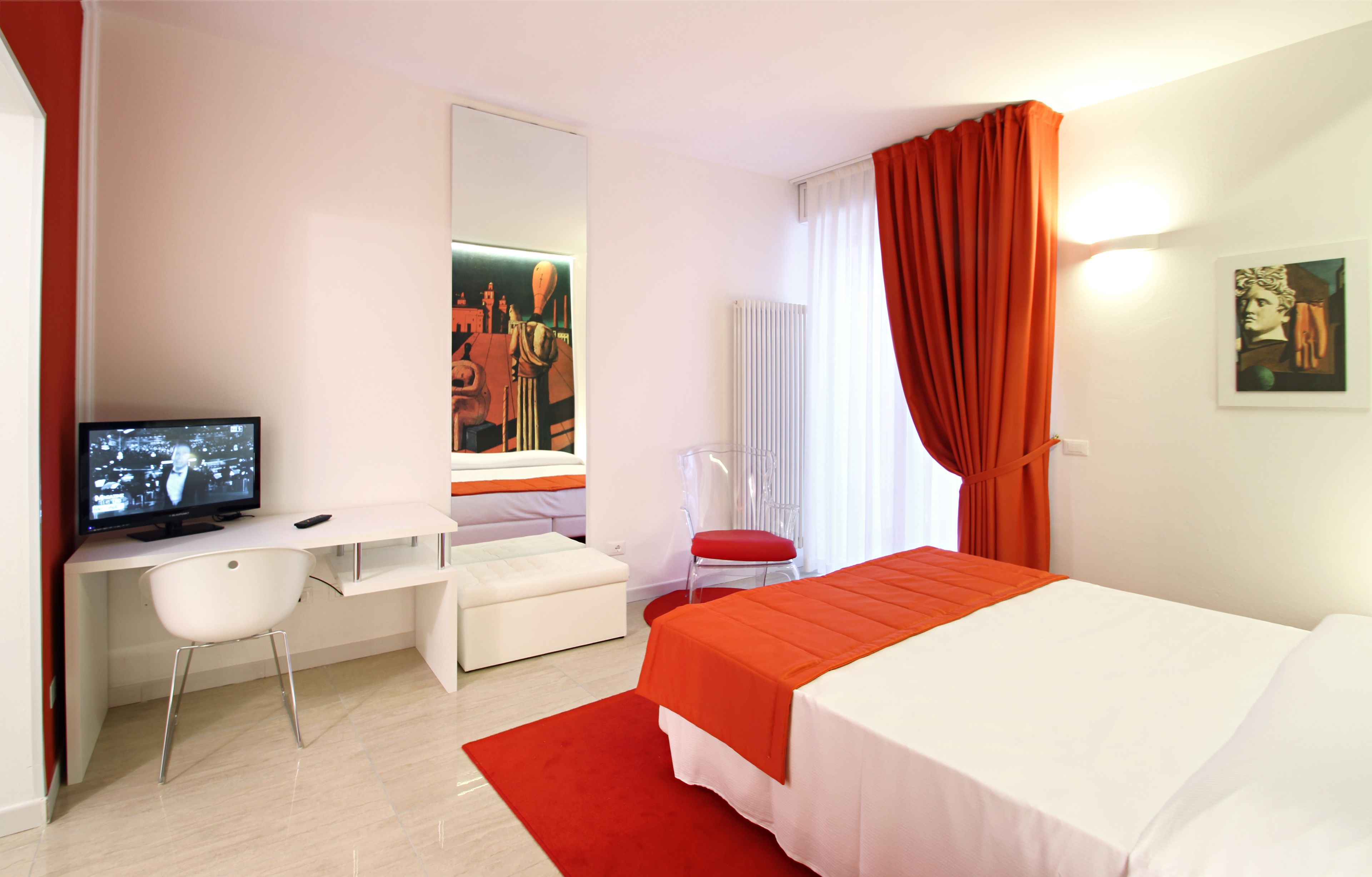 A modern hotel room with a bed, a desk, a chair, a television, and artwork on the walls.