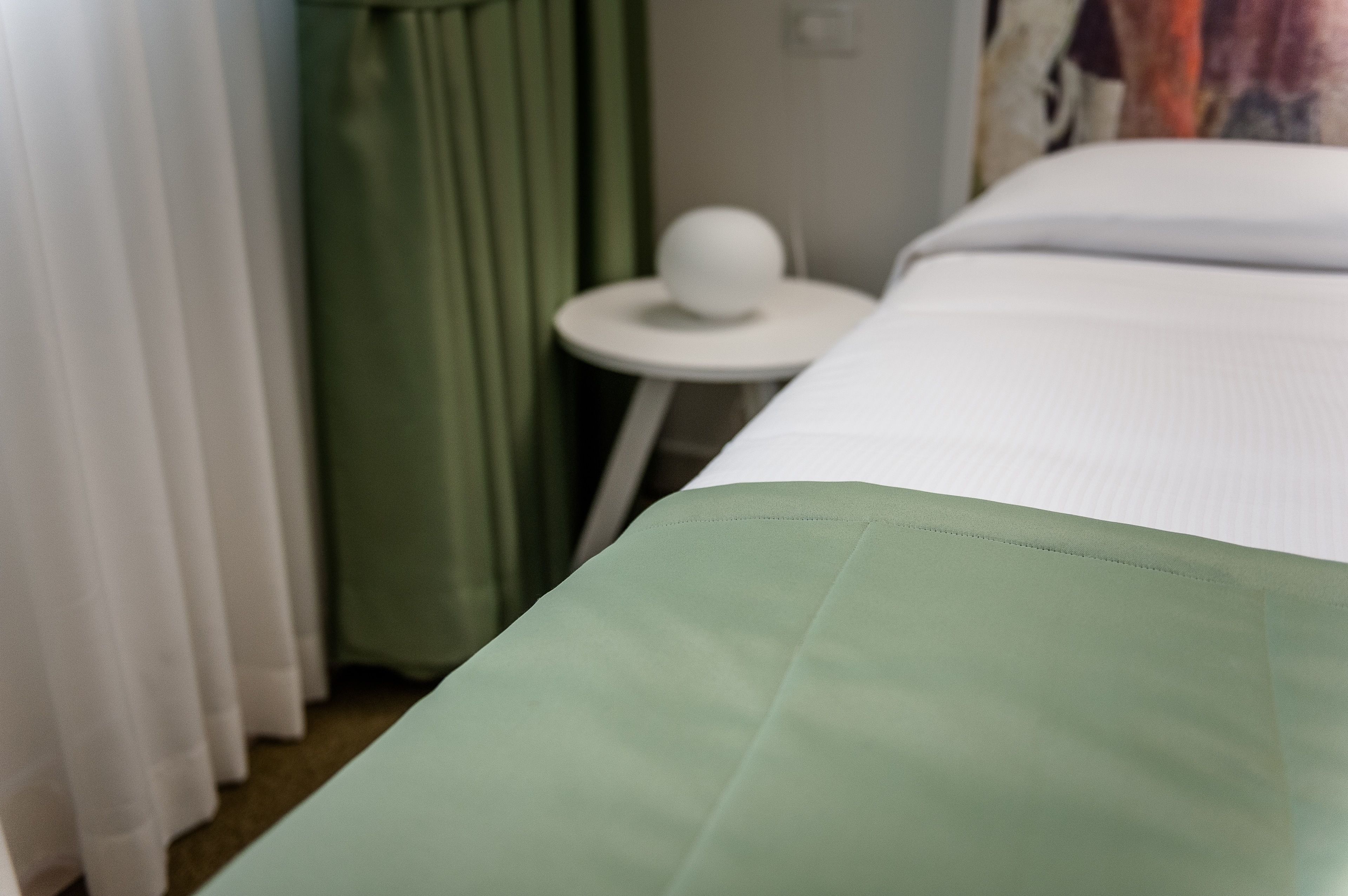 Una habitación de hotel con una cama, una mesita redonda con una silla blanca y una cortina verde.