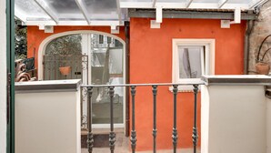 A covered outdoor area with a glass ceiling, a red wall, and a white door. - Ferrara Rooms (Ferrara)