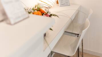 Un espace repas moderne avec une table et des chaises blanches, un menu posé sur la table et un arrangement floral en guise de décoration centrale.