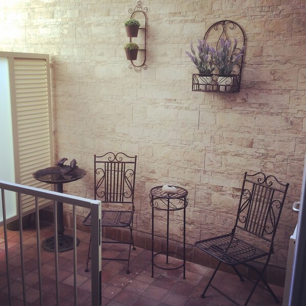 A small patio area with two metal chairs, a small table, and two wall-mounted planters with plants.