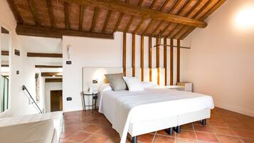 Camera da letto con soffitto in legno, un letto con biancheria bianca, un comodino con una lampada e vista su una porta che conduce in un'altra stanza.