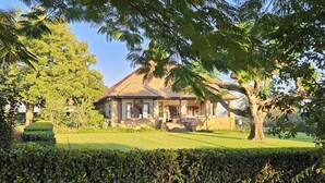 Una casa con un césped cuidado, un árbol grande al frente y un cielo despejado.