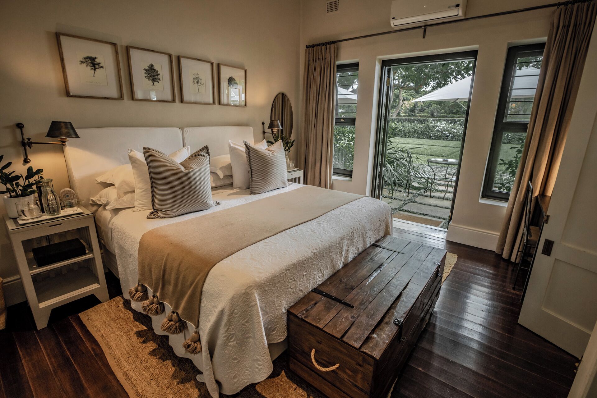 A bedroom with a bed, bedside tables, a wooden bench, and a view of the outdoors.