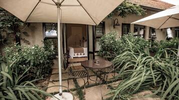 A patio with a table and chairs, surrounded by greenery and a building with windows.