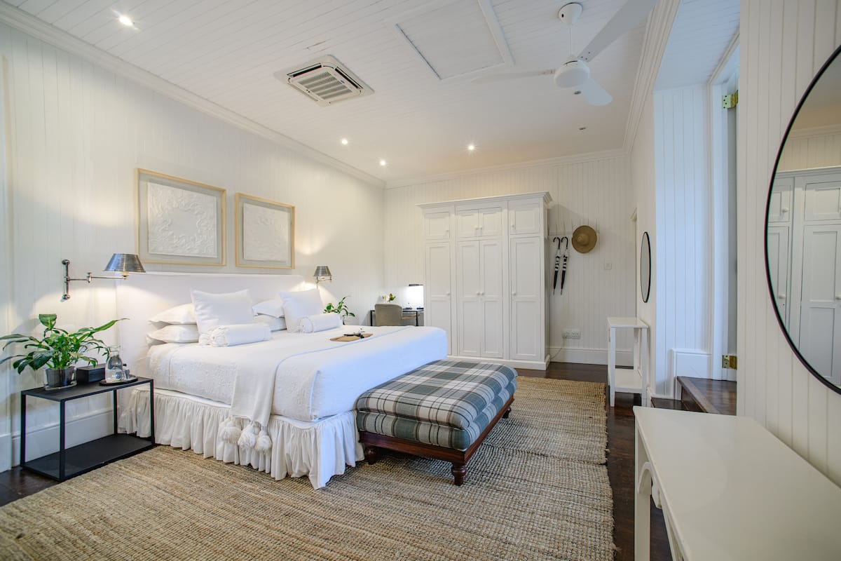 A bedroom with a large bed, bedside tables, a bench, a mirror, and built-in wardrobes.