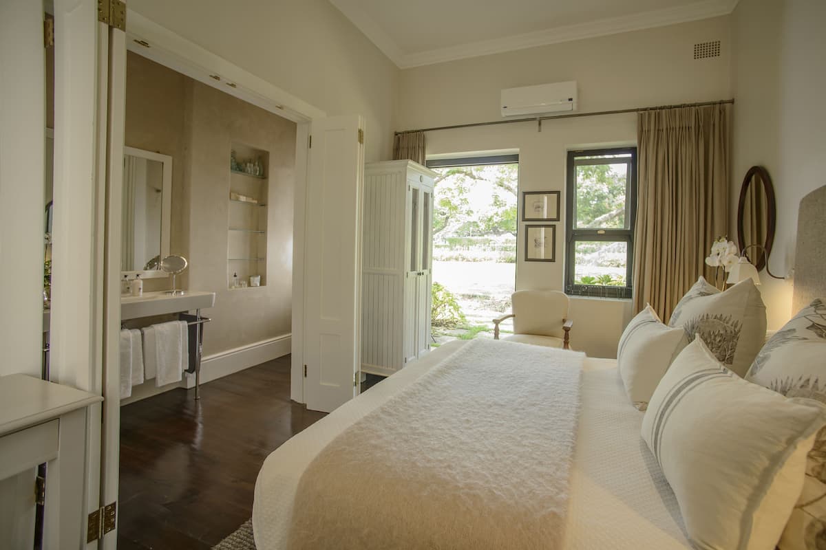 A bedroom with a large bed, a bathroom with a mirror, shelves, and a view of the outdoors.