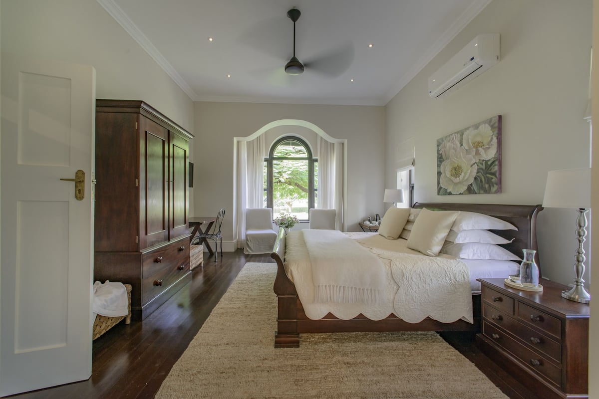 A bedroom with a large bed, a dresser, a vanity, and a window with curtains.