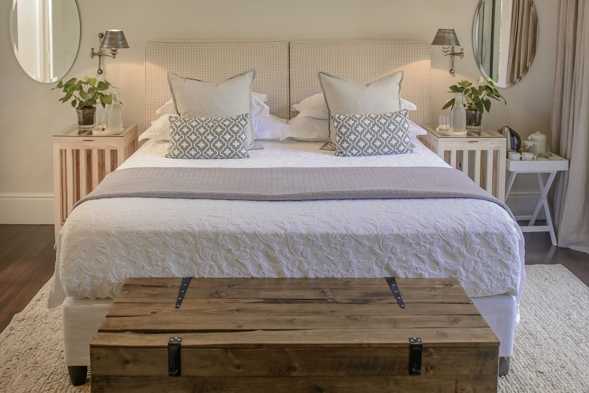 A neatly made bed with a wooden bench, two bedside tables with lamps, and a mirror on the wall.