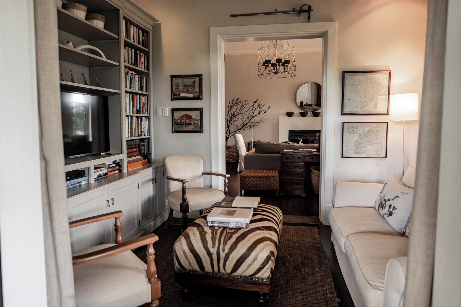 A cozy living room with a bookshelf, a television, a zebra-patterned ottoman, and a fireplace.