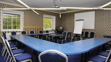 A conference room with a long table, chairs, a projector, a screen, and patterned wallpaper.