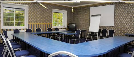 A conference room with a long table, chairs, a projector, a screen, and patterned wallpaper.