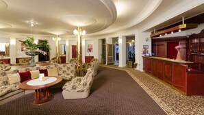 Un hall amplio con mostrador de recepción, sofás estampados, una mesa de centro y una planta decorativa.