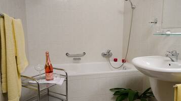 A bathroom with a bathtub, a shower, a sink, and a glass shelf with a bottle and glass.