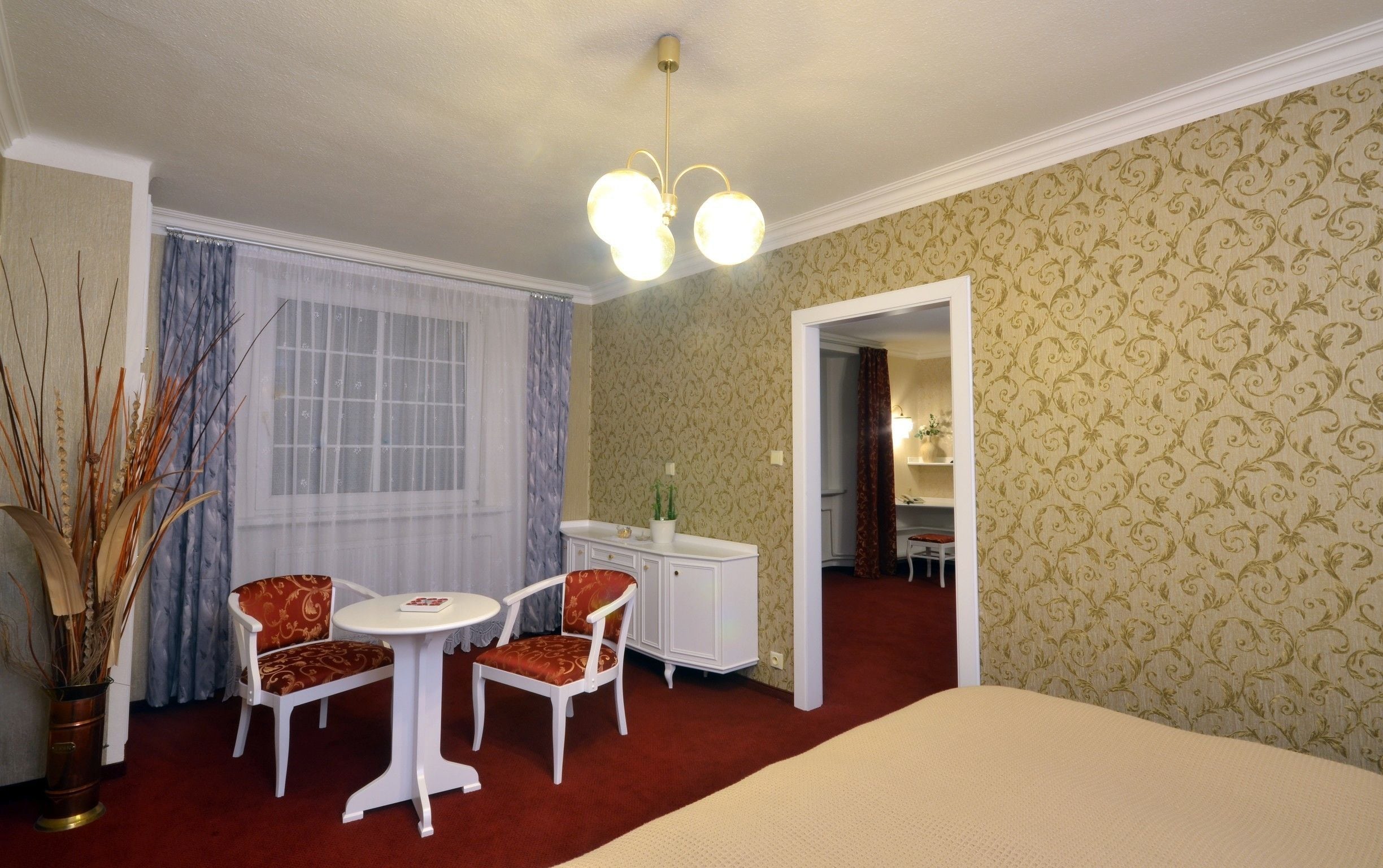 Una habitación de hotel con una cama, una mesita redonda pequeña con dos sillas, un tocador blanco y un espejo.