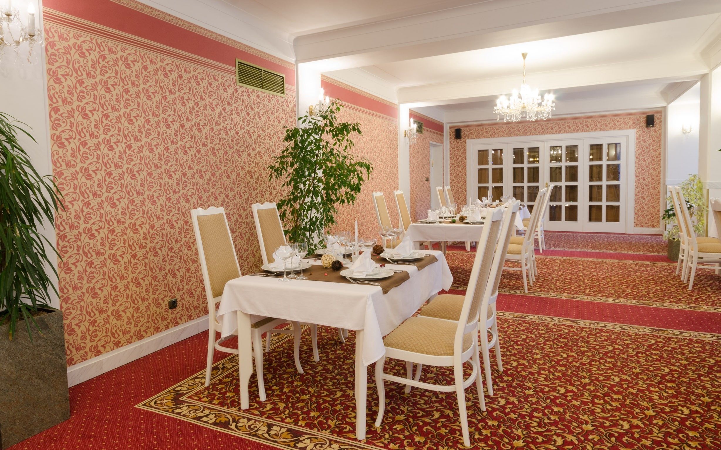 A dining area with a red carpet, white tablecloths, and white chairs.