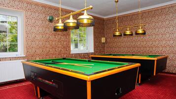 A pool room with two pool tables, patterned wallpaper, and a window with a view of greenery.