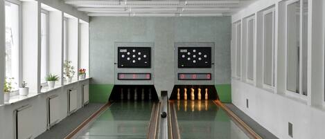 A bowling alley with two bowling lanes, green flooring, and white walls with windows.