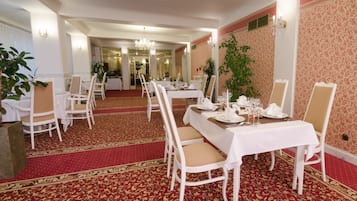 Un comedor formal con mesas y sillas blancas, piso con alfombra roja y una araña.